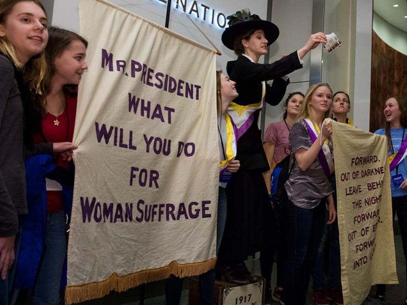 Visitors with suffrage banners standing with a suffragette historic re-enactor.